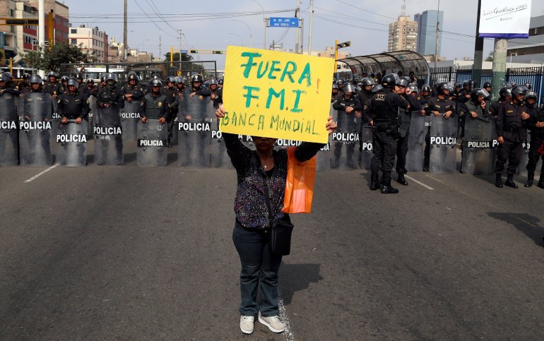 A protestor holds a sign that reads in Spanish "Get out IMF, World Bank" near police blocking protesters from getting any closer to the venue where the IMF and World Bank are holding their annual meetings in Lima, Peru, Friday, Oct. 9, 2015. More than 60 percent of Peruvians workers are in the informal economy, according to U.N. figures, spending on health care and education are below regional averages and most government revenues come not from income tax but rather taxes on sales and consumption, putting the burden disproportionately on the poor in the region with the world's most unequal wealth distribution. (AP Photo/Geraldo Caso Bizama)
